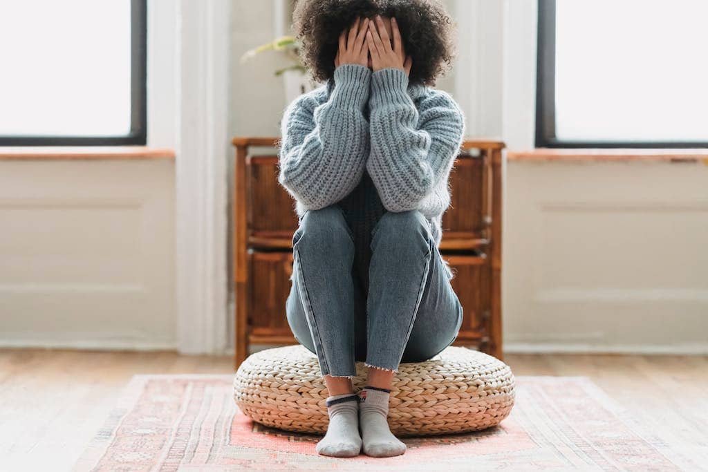 a woman sitting on a pouf with her hands over her face