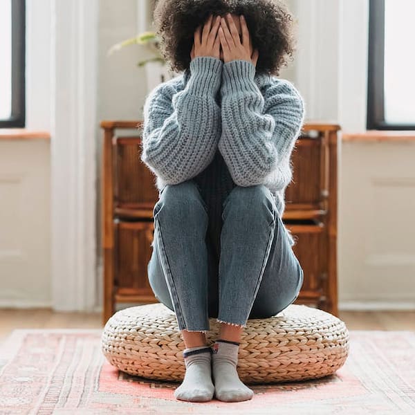 a woman sitting on a pouf with her hands over her face