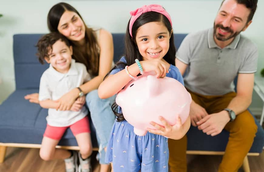 a group of people sitting on a couch and smiling at a girl holding a piggy bank- how to teach your kids about money